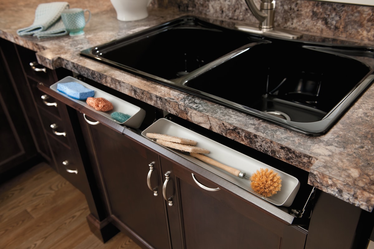 Flip-down drawer in front of a sink containing sponges.