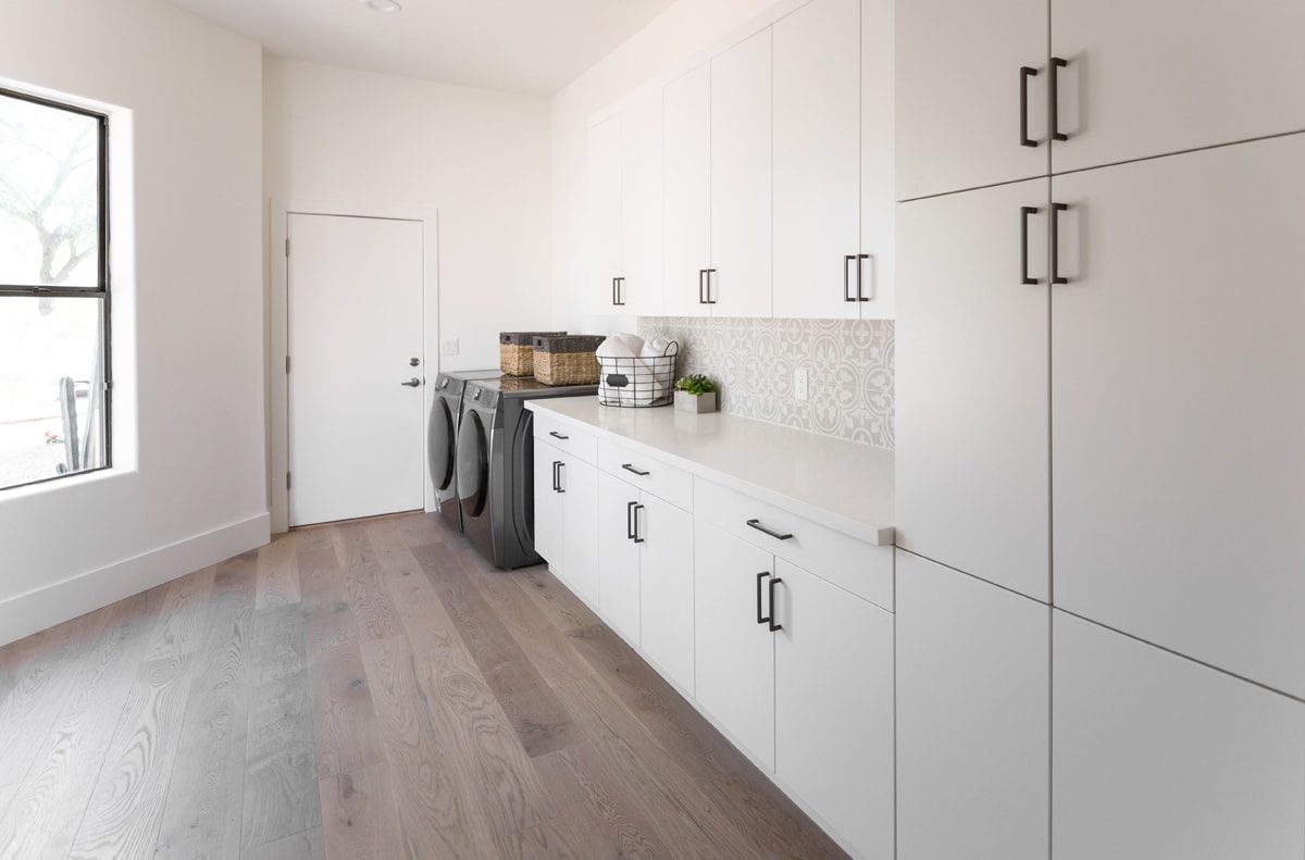 Laundry room with several white cabinets and a detailed white and beige tile backsplash.